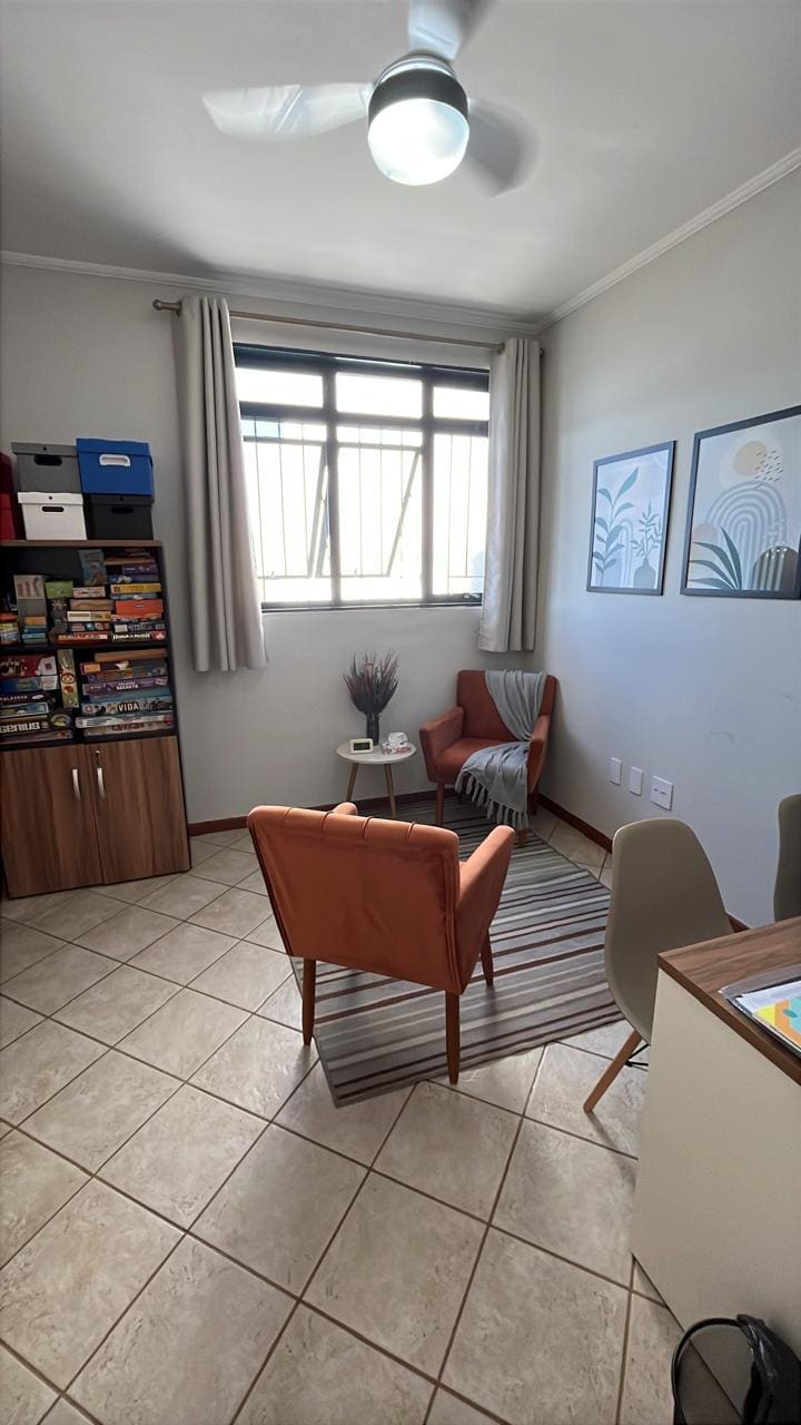 Sala do consultório com duas poltronas, estante de jogos e janela ampla